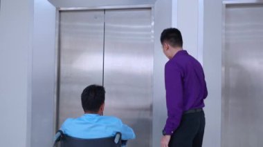 Genç Asyalı adam asansörle düğmeye basarken yaşlı baba hastanede tekerlekli sandalyede oturuyor, kıdemli baba ve oğlu tekerlekli sandalyeyle asansöre, sağlık ve sigortaya gidiyor..