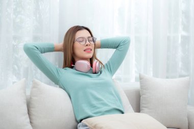 Gözlüklü genç Asyalı kadın evdeki oturma odasında rahatlamak ve rahatlamak için kanepede oturuyor. Rahat ve dinlenen bir kadın, yaşam tarzı ve ev hayatı kavramı..