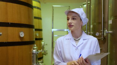 Şarap üreticisi kadın şaraphanedeki şarap üretimini kontrol ediyor ve inceliyor, müfettiş kaliteyi kontrol ediyor ve şarap deposunu oda veya fıçıda mayalıyor, endüstriyel ve imalat konseptini inceliyor..