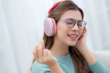 Kulaklık takmış, müzik dinleyen mutlu genç bir kadın. Oturma odasında eğleniyor ve eğleniyor. Eğlence dolu mutlu bir kadın, bir kişi, yaşam tarzı konsepti..