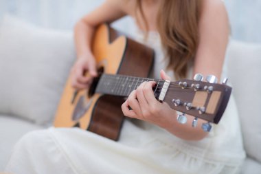 Genç Asyalı bir kadının evdeki kanepede oturup gitar çalması, yetenek ve pratik yapması, gitarist ve hobisi zevkli ve rahatlatıcı, eğlence ve yaşam tarzı..