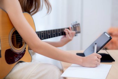 Yakından bakan kadın kanepeye oturup pratik yapmak için oturma odasında gitarlı bir şarkı besteledi. İnternette müzik ve gitar öğrenme hakkında ders izleyen kadın, yaşam tarzı konsepti..