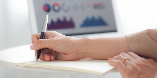 Closeup hands of businesswoman writing and using laptop computer on desk for calculate and planning investment and finance at home, female inspecting information report and stock, business concept.