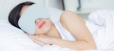 Güzel Asyalı genç bir kadın örtülü göz takıyor ve yatak odasında başı yastıkta uyuyor rahatlık ve mutlulukla, rahatlık ve rahatlık için boş vakti olan bir kız, yaşam tarzı konsepti..