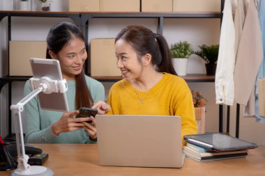 Başarı ve neşeli, girişimci veya çevrimiçi satıcı, ecommerce veya startup business, küçük işletme ile mağaza incelemesi için tablet ve dizüstü bilgisayar kullanan iki genç Asyalı kadın.