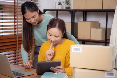 Tablet üzerinde çalışan iki genç Asyalı kadın çevrimiçi işleri yönetir ve planlarken ve evde siparişleri kontrol ederken, girişimci ve küçük işletme, çevrimiçi satıcı ile perakende satış, girişim işi.