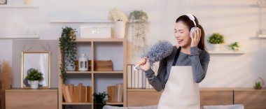 Genç Asyalı bir kadın, kulaklıkla müzik dinlerken, oturma odasında temizlik yaparken, ev işi yaparken, evde toz alırken, şarkı söylerken, ev işi yaparken, yaşam tarzı konsepti.
