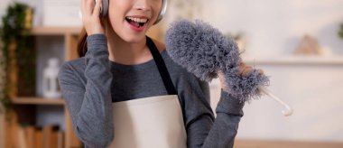 Genç Asyalı bir kadın, kulaklıkla müzik dinlerken, oturma odasında temizlik yaparken, ev işi yaparken, evde toz alırken, şarkı söylerken, ev işi yaparken, yaşam tarzı konsepti.