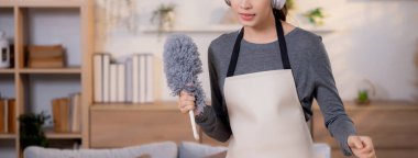 Genç Asyalı bir kadın, kulaklıkla müzik dinlerken, oturma odasında temizlik yaparken, ev işi yaparken, evde toz alırken, şarkı söylerken, ev işi yaparken, yaşam tarzı konsepti.