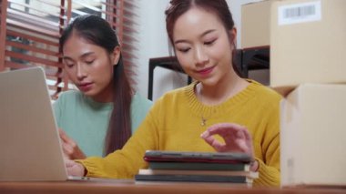 Başarı ve neşeli, girişimci veya çevrimiçi satıcı, ecommerce veya startup business, küçük işletme ile mağaza incelemesi için tablet ve dizüstü bilgisayar kullanan iki genç Asyalı kadın.