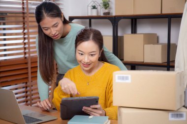 Tablet üzerinde çalışan iki genç Asyalı kadın çevrimiçi işleri yönetir ve planlarken ve evde siparişleri kontrol ederken, girişimci ve küçük işletme, çevrimiçi satıcı ile perakende satış, girişim işi.