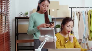 Tablet üzerinde çalışan iki genç Asyalı kadın çevrimiçi iş yaparken ve planlarken ve akıllı telefondaki konuşmayla siparişleri kontrol ederken, çevrimiçi satıcı, girişim şirketi ve kargoyla perakende satış yaparken.