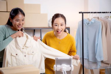 İki genç Asyalı kadın online giyim mağazasında yaşarken, evde sosyal tabletle giysi satışı yaparken, girişimci çevrimiçi kıyafet satışı ve sunumu için çevrimiçi satış yapıyor..