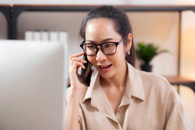 Genç Asyalı iş kadını ofis telefonuyla konuşurken masaüstü bilgisayarı kullanıyor, iş kadını telefon, iş ya da danışmanlık yaparken masaüstü bilgisayarıyla çalışıyor.