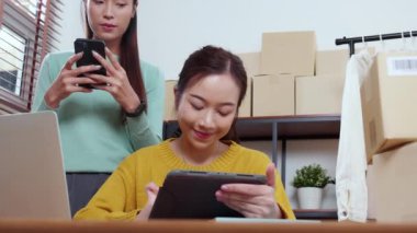 Tablet üzerinde çalışan iki genç Asyalı kadın çevrimiçi iş yaparken ve planlarken ve akıllı telefondaki konuşmayla siparişleri kontrol ederken, çevrimiçi satıcı, girişim şirketi ve kargoyla perakende satış yaparken.