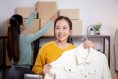 İki genç Asyalı kadın online giyim mağazasında yaşarken, evde sosyal tabletle giysi satışı yaparken, girişimci çevrimiçi kıyafet satışı ve sunumu için çevrimiçi satış yapıyor..