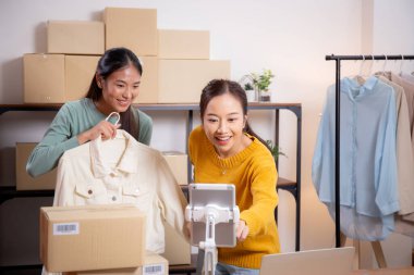 İki genç Asyalı kadın online giyim mağazasında yaşarken, evde sosyal tabletle giysi satışı yaparken, girişimci çevrimiçi kıyafet satışı ve sunumu için çevrimiçi satış yapıyor..