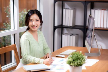 Masaüstü bilgisayarıyla çalışan Asyalı genç iş kadını portresi modern ofis binasında finansal planlama yaparken, iş kadını çalışma, iş ve finans hakkında planlar yapıyor..