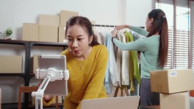 İki genç Asyalı kadın online giyim mağazasında yaşarken, evde sosyal tabletle giysi satışı yaparken, girişimci çevrimiçi kıyafet satışı ve sunumu için çevrimiçi satış yapıyor..