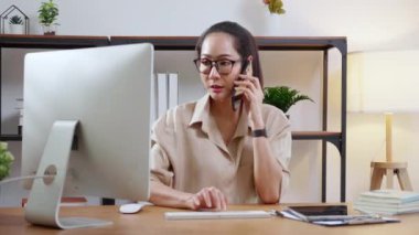 Genç Asyalı iş kadını ofis telefonuyla konuşurken masaüstü bilgisayarı kullanıyor, iş kadını telefon, iş ya da danışmanlık yaparken masaüstü bilgisayarıyla çalışıyor.