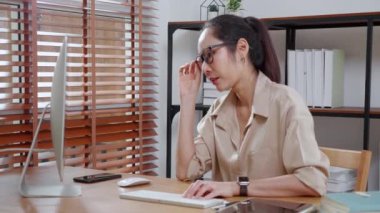 Genç Asyalı iş kadını masaüstü bilgisayarını kullanırken modern ev ofisin başarısı için düşünüyor, bilgisayar jestleriyle çalışan iş kadını evde, iş yerinde ve serbest oturma odasında olmaktan memnun..
