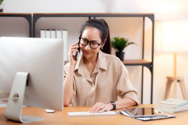 Genç Asyalı iş kadını ofis telefonuyla konuşurken masaüstü bilgisayarı kullanıyor, iş kadını telefon, iş ya da danışmanlık yaparken masaüstü bilgisayarıyla çalışıyor.