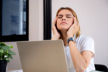 Mutsuz Kafkasyalı genç iş kadını masadaki dizüstü bilgisayarını kullanıyor. Ofiste stresli ve bitkin durumda. İş kadını hayal kırıklığına uğramış ve kaygılı bir şekilde dizüstü bilgisayarda çalışıyor..