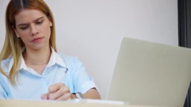 Kafkasyalı genç iş kadını laptop bilgisayar kullanıyor. Stres sırasında masa başında belgeye bakıyor. İş kadını, düşünceli ve hayal kırıklığına uğramış bir not defteri kullanıyor..