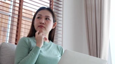 Genç Asyalı iş kadını laptopla çalışırken düşünceli bir şekilde ofisteki koltukta oturuyor, iş kadını evdeki not defterini kullanıyor, kadın dizüstü bilgisayarla düşünüyor..