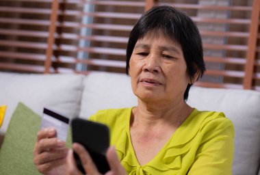 Kıdemli Asyalı kadın internet üzerinden akıllı telefon alışverişi yapıyor. İnternete kredi kartı alıyor. Akıllı telefon, alım-satım, ödeme, iş ve finans ile kadın ödemesi yapıyor..
