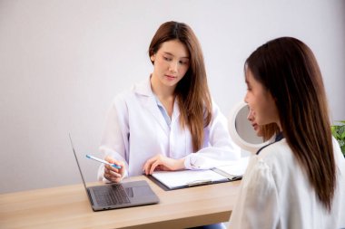 Genç Asyalı hasta kadın, modern tıp ofisinde dizüstü bilgisayar seyrederken, cilt ve kırışıklıkları hakkında doktorlara danışmanlık yapıyor, doktor yüz tanılama ve açıklama yapıyor..