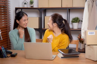 Başarı ve neşeli, girişimci veya çevrimiçi satıcı, ecommerce veya startup business, küçük işletme ile mağaza incelemesi için tablet ve dizüstü bilgisayar kullanan iki genç Asyalı kadın.