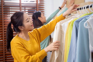 Hazırlık teslimatı için mağazada kıyafet düzenleyen iki genç Asyalı kadın, satıcı seçici giysiler, perakende satış için seçici giysiler, teslimat için mal, küçük işletme.