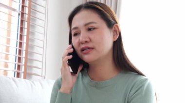 Genç Asyalı iş kadını telefonda gülümsüyor ve rahatlıyor. Oturma odasındaki koltukta oturuyor, akıllı telefonuyla konuşan neşeli bir kadın evde koltukta oturuyor, yaşam tarzı ve iletişim kuruyor..