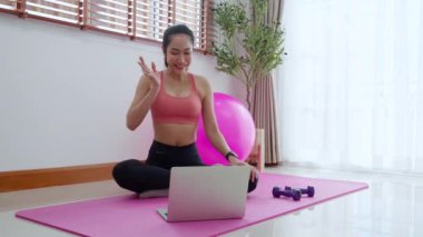 Genç Asyalı bir kadın arkadaşlarıyla yoga yaptıktan sonra evde dinlenmek için antreman yaparken görüntülü konuşma yapıyor. Antrenman ve egzersiz sonrası not defterini konferans, spor ve refah için kullanan bir kadın..