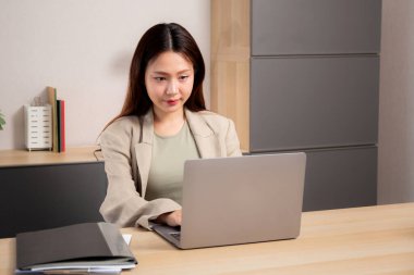 Genç Asyalı bir kadın modern ofiste başarılı olmak için dizüstü bilgisayar planlaması yapıyor, iş kadını kendine güvenen, masa başında çalışan, iş konsepti olan bir not defteri yazıyor ve izliyor..