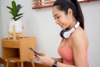 Antrenman için akıllı telefon izleyen genç Asyalı kadın yoga ve oturma odasında egzersiz yapıyor. Akıllı telefonla sohbet botu kullanan kadın. Egzersiz, spor ve refah için yapay zeka kullanıyor..
