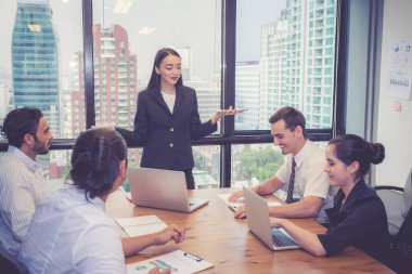 Grup iş adamları takım olarak toplanırken, kadın modern ofiste planlama ve strateji pazarlaması, beyin fırtınası ve takım çalışması, iş dünyası konsepti sunumu ve stratejisi hakkında açıklama yapıyor..