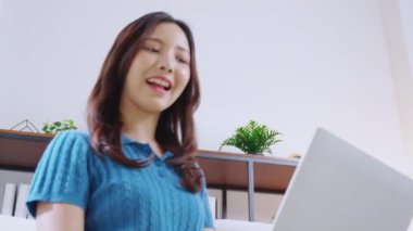 Kanepede oturan Asyalı genç bir kadın evdeki oturma odasında dizüstü bilgisayar kullanıyor, sosyal medyayı internet üzerinden sohbet ve sohbet için kullanıyor, yaşam tarzı kavramı..