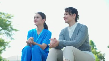 Genç Kafkasyalı hemşire dışarıda parktaki üzgün bir hastayla ilgileniyor ve onu rahatlatıyor, doktor kadın desteği ve hasta, bakıcı ve hizmeti ile yaşlı, medikal ve teselli ediyor..