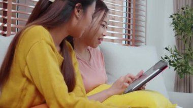 Kanepede oturan iki genç Asyalı kadın internet üzerinden tablet bilgisayar alışverişi yapıyor. İnternete kredi kartı satın alıyor, iş, alım ve ödeme, iş ve finans ile kadın ödemesi yapıyor..