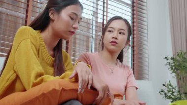 Genç Asyalı bir kadın, arkadaşını ağlama ve depresyonla rahatlatırken oturma odasında kanepede oturuyor, arkadaşlığın sıkıntısı ve empatisi, umutsuzluk ve ruh sağlığını desteklerken, bir kadın da arkadaşını teşvik ediyor..