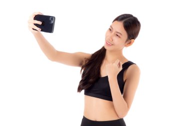 Spor giyinen genç Asyalı kadın portresi ve akıllı telefondaki selfie izole edilmiş beyaz arka plan, spor giyimli kız akıllı telefon, spor ve sağlık hizmetlerinde fotoğraf çekiyor..