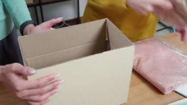 Kapalı el, karton kutuya paketlenmiş bir kadın, nakliye veya depolama için ev ofisinde, çevrimiçi satıcı teslimat için giysileri kutuda paketliyor, lojistik ve kargo, perakende hizmeti.