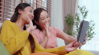Oturma odasında dijital tablet kullanan iki genç Asyalı kadın, sosyal medyayı internet tableti ve konuşma mesafesi için kullanan kadın, yaşam tarzı kavramı.