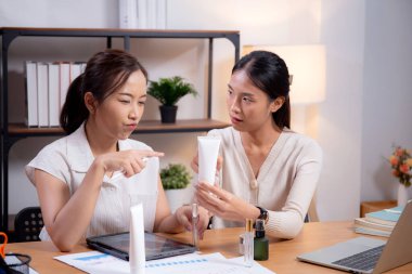 Ofiste kozmetik ürünü ya da kremi test eden ve araştıran iki Asyalı iş kadını. Cilt tasarımı, geliştirme ve iş dünyasından iki iş kadını..