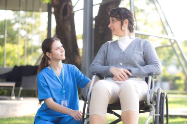 Kafkasyalı genç hemşire dışarıda tekerlekli sandalyede otururken hastayla rahatlıyor, doktor kadın desteği ve hasta ile danışmanlık yapıyor, yaşlı, tıbbi ve teselliye hizmet veriyor..