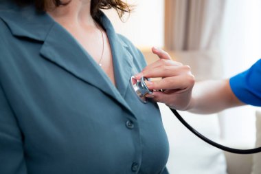 Bakıcı genç hemşire. Steteskoplu kadını muayene ediyor. Oturma odasındaki kanepede oturuyor..