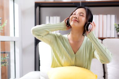Mutlu genç Asyalı kadın kulaklık takıyor, kanepeye oturmuş müzik dinliyor ve evde eğleniyor, eğlence dolu mutlu bir kadın, bir kişi, yaşam tarzı konsepti.
