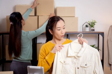 İki genç Asyalı kadın online giyim mağazasında yaşarken, evde sosyal tabletle giysi satışı yaparken, girişimci çevrimiçi kıyafet satışı ve sunumu için çevrimiçi satış yapıyor..